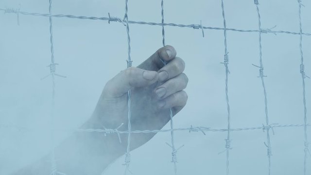 Hand Grasps Wire Fence With Smoke Passing