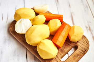 peeled raw potatoes, carrots, onions on a wooden background. Preparing vegetables for cooking.