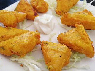 Close up paneer cheese fried in batter is on a platter with white sauce and herbs