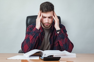 Upset man looks at a calculator. Guy is upset at the big expense. Human is holding his head. Man rereads the contract. Concept - guy is studying a loan agreement. Concept - thinks how to cut costs.