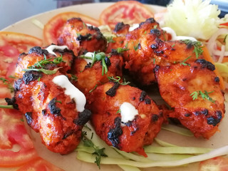 Close-up view of an Indian dish chicken Tikka tandoori, laid out on rings of tomatoes and garnished with salad