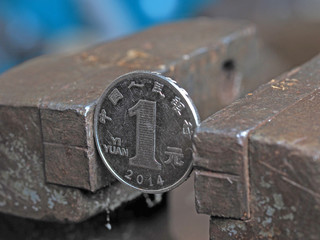 Yuan coin clamped in a metal vise. Currency under the onslaught, the concept of financial problems and crisis