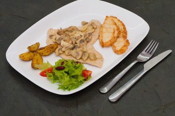 Stewed mushrooms with fish fillet, salad, fried potatoes and croutons, on a warm gray background. Tasty traditional italian food