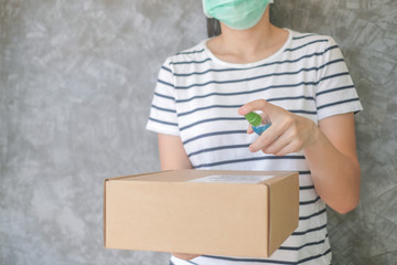 Asian woman wears mask using spray alcohol sanitizer cleaning parcel post, to prevent the virus and...