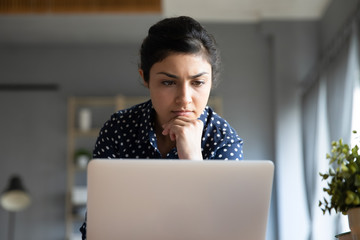 Head shot close up concentrated young indian woman looking at laptop monitor. Focused millennial...