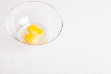 Two broken eggs in a glass transparent bowl on a white table close-up isolated for making an omelet or the main ingredient for baking desserts or dough.