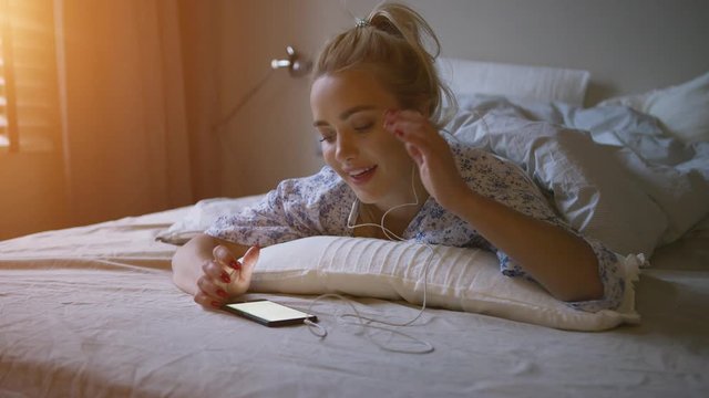 Charming young woman with ponytail listening to good music while lying on comfortable bed