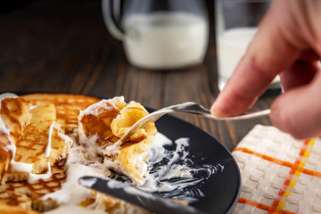 Breakfast, golden pancakes folded on a gray plate, hand holds a fork over a dish, milk in a decanter and glass, rustic style, dim light, shallow depth of field, selective focus.