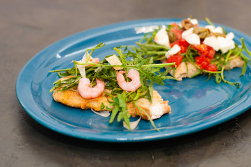 Bruschetta with shrimp, arugula, tomatoes, cheese and sauce, closeup, on gray background, high Italian cuisine