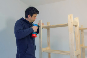 Portrait of man screwing parts with bolts using electric screwdriver collecting rack furniture....