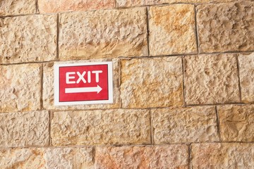 Fototapeta na wymiar Red exit sign on sandstone textured wall background