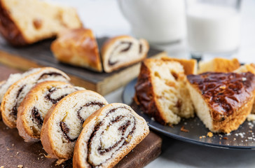 Pie with poppy seeds sliced into pieces, on wooden boards and in a dish, a glass and a jug with milk, selective focus, shallow depth of field, light background, top lighting.