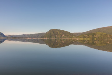 Norwegian fjord and mountains surrounded by clouds, midnight sun, polar day, ideal fjord reflection in clear water. selective focus.