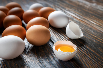 White and brown farm eggs lie on a wooden table, close-up, low light, selective focus, shallow depth of field. Organic food concept