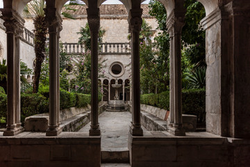 Botanical garden with greenery of the 13th Century Franciscan Monastery cloister in the Old Town of Dubrovnik, Dalmatia, Croatia. Romanesque gothic style. Decorative columns and a fountain