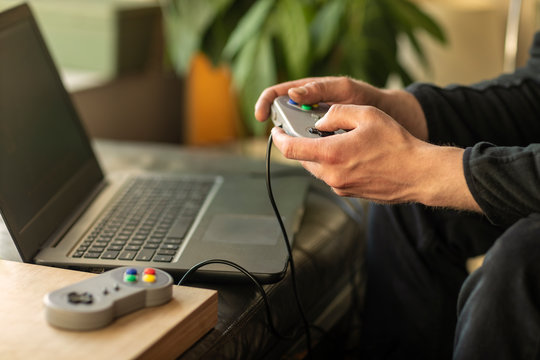 A man playing on his laptop computer with a old school classic gaming console feeling nostalgic at home during lockdown time in 2020