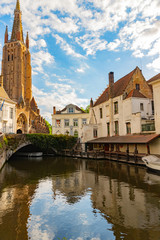 Fototapeta na wymiar View of Dijver canal with canal boat, vine covered bridge, traditional buildings and Notre Dame Cathedral in Bruges, Belgium
