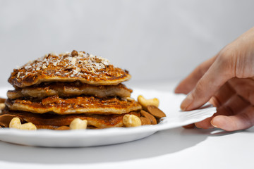 Close-up of female hand taking white plate with homemade american vegan pancakes with cashew and almond nuts.