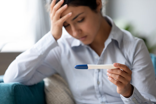 Focus on pregnancy test in hands of frustrated stressed young indian woman. Unhappy depressed millennial hindu girl dissatisfied with result, unwanted pregnancy, fertility problem, bad news concept.