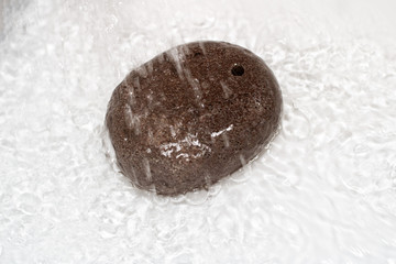 Spa pumice oval shaped under a stream of water on a white background. Home Body Care Supplies