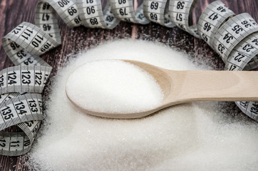 sugar and measuring tape on a wooden background. The concept of weight loss, diet.