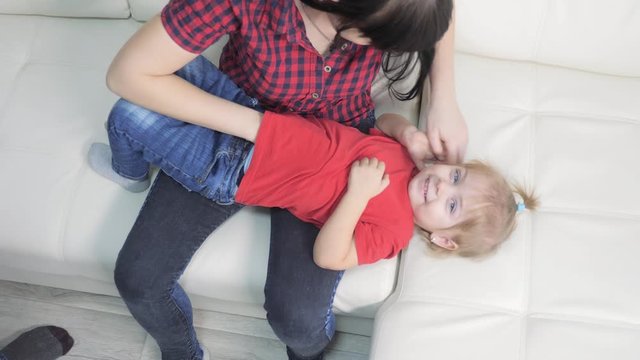 happy family little girl laughs from lifestyle tickling. woman playing with daughter indoors a happy family laughing
