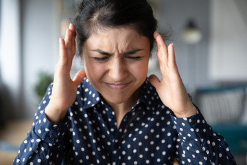 Head shot close up millennial indian overload woman suffering from strong head ache or loud noises....