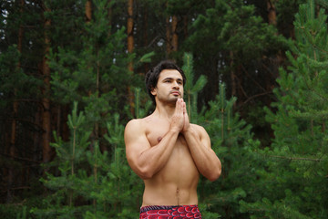 Healthy lifestyle, sport, yoga and people concept - handsome young man doing yoga over green woods background
