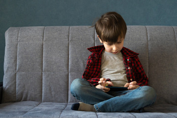 Focused boy enthusiastically plays in a smartphone. Leisure during self-isolation concept. Gadget...