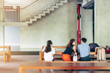 Back view of Asian master degree students work and consult while staying on the first floor below the school building in the afternoon.