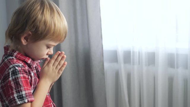 little son boy prays bedtime religion concept. prayer child indoors praying by lifestyle bed in front of window