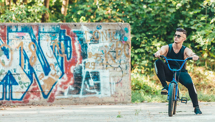 Young handsome hipster man posing outdoor on the street having fun with bmx bicycle. graffiti wall background
