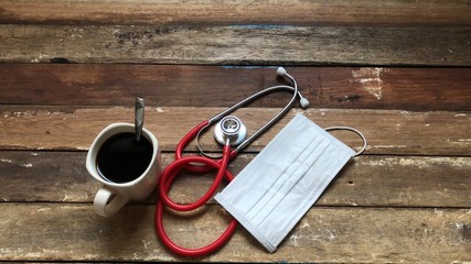 Stethoscope,Medical Cardiologist,Mug coffee and hygiene surgical on old wood table top,dimly light,free space for your text,Corona epidemic.Concept of Health care and prevent covid-19.