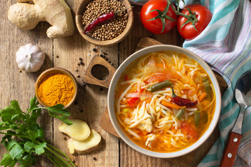 Tukpa soup of Indian cuisine. Hot noodle soup with chicken, ginger, cilantro and spices on a deyven wooden table. Top view flat lay background.