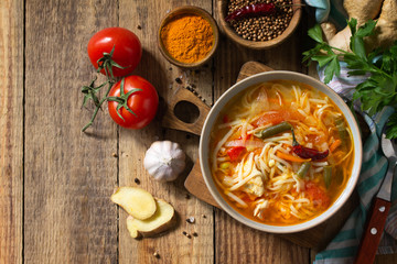 Tukpa soup of Indian cuisine. Hot noodle soup with chicken, ginger, cilantro and spices on a deyven wooden table. Top view flat lay background. Copy space.