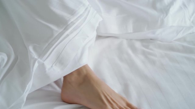Closeup of female couple play and dance their feet under blanket while wake up in bed in morning in slow motion