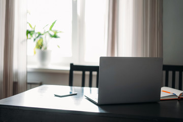 Opened laptop notebook on black table with mobile phone and notes against window at the home