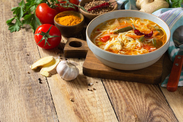 Tukpa soup of Indian cuisine. Hot noodle soup with chicken, ginger, cilantro and spices on a deyven wooden table. Copy space.