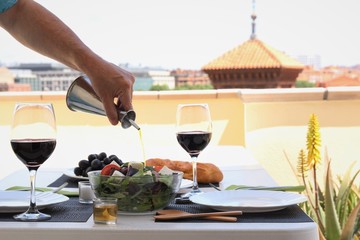 Hand of man pouring olive oil to salad bowl preparing table for lunch at terrace. photo 