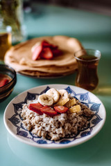 Pancakes and oatmeal with strawberries, banana honey. Healthy organic food. Tasty breakfast on a blue background with lilacs. Soft focus