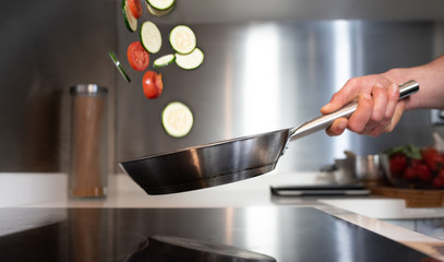 Close up of hand with skillet sauteing vegetables throwing in the air.