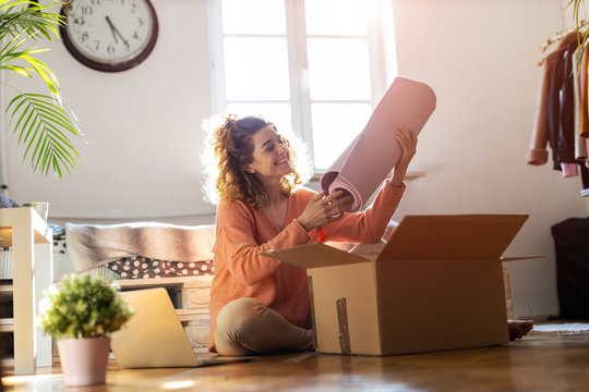 Woman Unpacking Box With Workout Equipment At Home 
