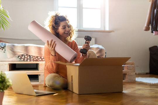 Woman Unpacking Box With Workout Equipment At Home 
