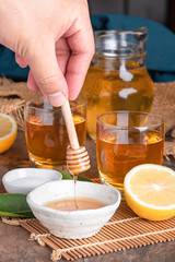 A glass of iced tea with mint and lemon on a wooden table.A glass cup of tea with lemon, mint, and honey on a wooden rustic table.