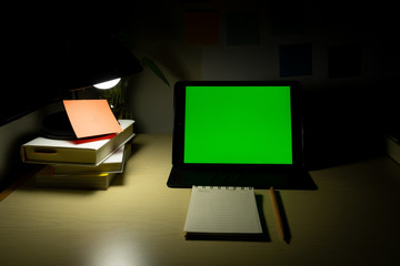 Tablet with blank chroma green screen places on studying desk with books and stationary beside....