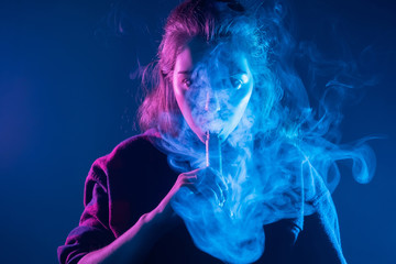 Smoking an electronic cigarette. The girl's face is covered with smoke from vape. Portrait of a...