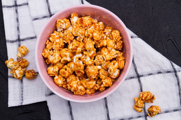 Close-up golden fried popcorn in ceramic plate on checkered background. From top view. Concept of homemade popcorn and watching tv at home.