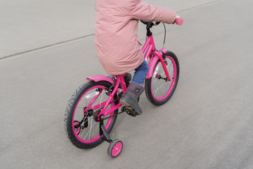A child rides a bicycle in a pink jacket. A child with his back to the photographer. Spring walks near the house on the bike.