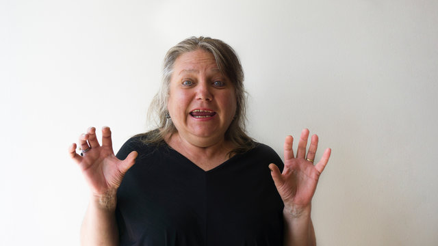 Scared Old Woman With Green Eyes Smiling At Camera. One Beautiful Green Eyed Elder Woman With Panic Attack Concept. Modern Blonde Lady With Casual Hair Isolated On White Wall Background.