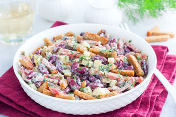 Salad with red beans, smoked sausage, cheese and crackers in a white bowl, horizontal